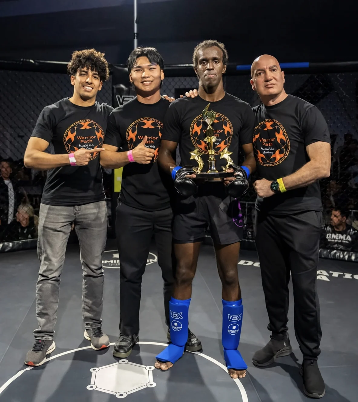 The four Build My Idea team members together at a martial arts event, holding a trophy